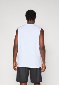 Chemise blanche sans manches avec un col rond, assortie à un short en maille noir, mettant en avant une coupe décontractée et une texture de tissu lisse.