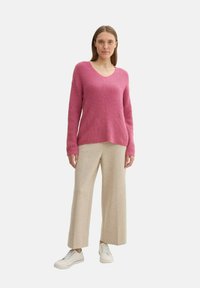 Maglione rosa a V con texture a coste e motivi diagonali, abbinato a pantaloni beige a gamba larga e sneakers bianche.
