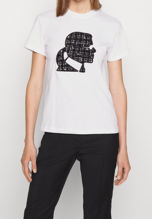 Camiseta blanca de algodón con un diseño de silueta negra y un patrón texturizado. Manga corta y cuello redondo.