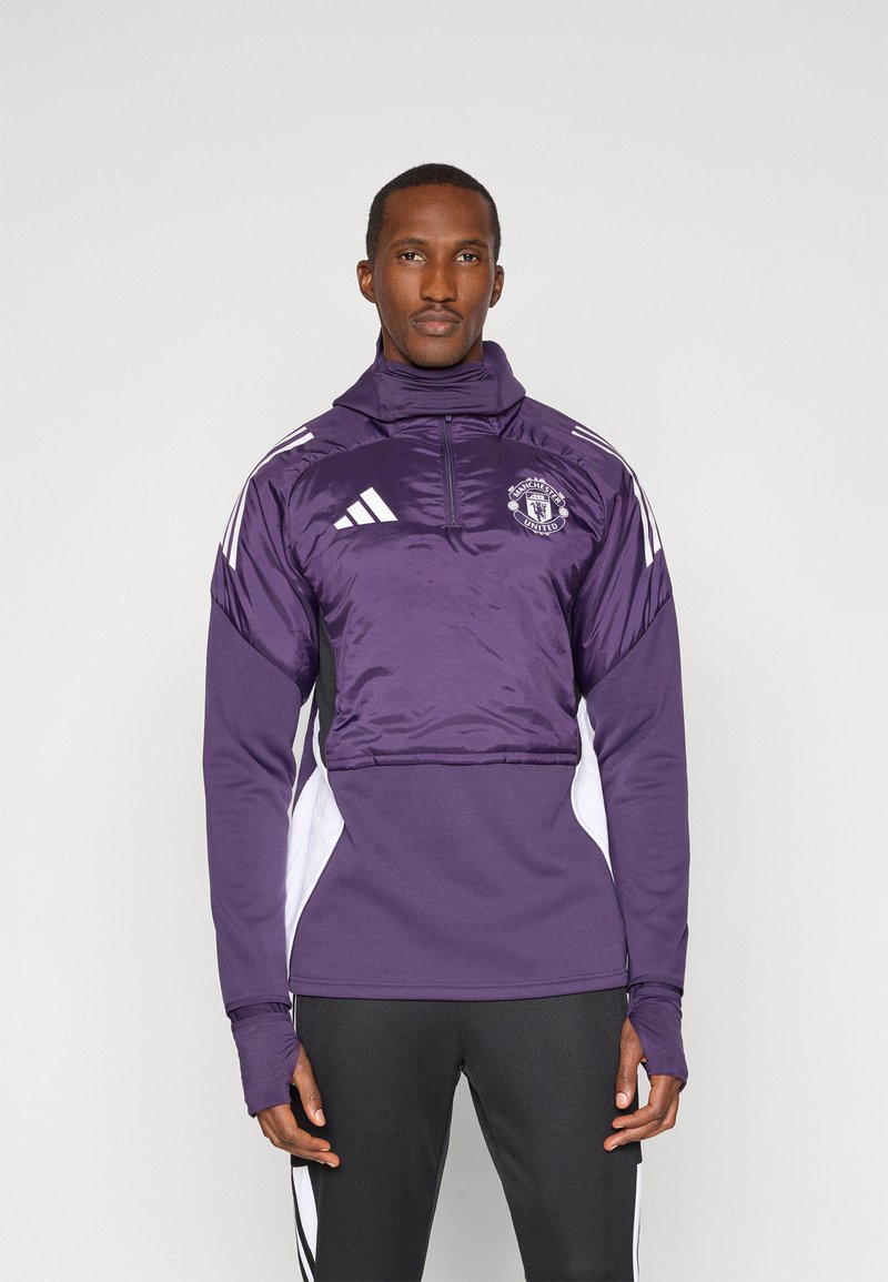 Lilla træningsjakke med høj krave, lynlåslukning foran, hvide sidestykker og Manchester United-logo; har tekstureret stof og lange ærmer.