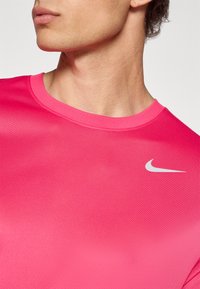 Różowa koszulka sportowa z krótkim rękawem i okrągłym dekoltem. Posiada gładki, lekki materiał oraz małe białe logo Nike na piersi.
