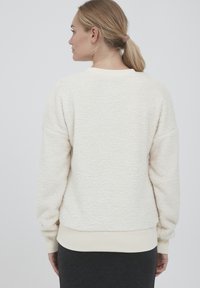 Fleece sweatshirt i off-white, med en teksturert overflate, ribbede mansjetter og rund halslinning. Synlige sømdetaljer langs ryggen.