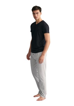 Schwarzes Baumwoll-T-Shirt mit kurzen Ärmeln und V-Ausschnitt sowie hellgraue Baumwoll-Schlafanzughosen. Slim Fit mit Seitentaschen. Modell steht barfuß.