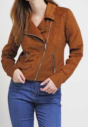 Veste de moto en daim marron avec une fermeture éclair diagonale, un col plat, des poches latérales et des manches texturées, assortie à un jean bleu.