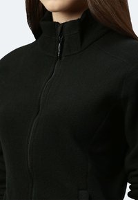Giacca in fleece nera con colletto alto, zip intera e tessuto testurizzato. Il design include tasche laterali per una maggiore funzionalità.