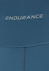 Blauwe zwemkleding met het woord "ENDURANCE" in zilver gedrukt. Kenmerkt zich door een gladde textuur en platte naden voor comfort en duurzaamheid.
