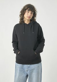 Schwarzer Hoodie mit einer Vordertasche, Kordelzugkapuze, gerippten Bündchen und einer lockeren Passform, kombiniert mit hellblauen Jeans.