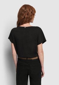 Schwarzes, kurz geschnittenes T-Shirt aus weichem Stoff, mit kurzen Ärmeln und rundem Halsausschnitt. Besonderes Merkmal: ein kleines Logo auf der Rückseite.