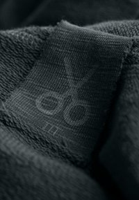 Tessuto nero con una superficie texture; presenta un'etichetta con un logo a forbice sottile, che indica il materiale o l'identità del marchio.