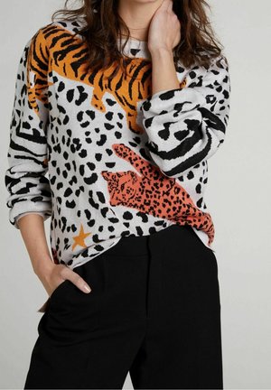 Suéter de punto con una mezcla de estampados de animales en naranja, negro y blanco, con un acabado texturizado y un corte holgado, combinado con pantalones negros.