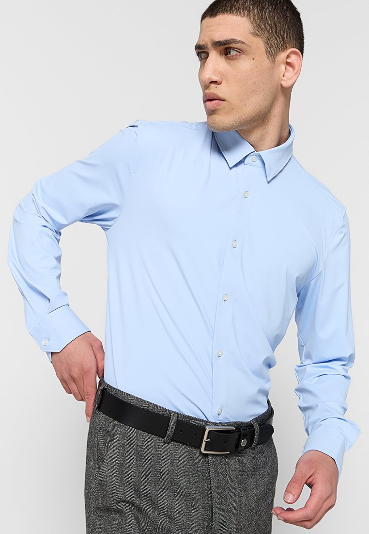 Chemise de couleur bleu clair avec un col pointu et un devant à boutons ; tissu lisse ; manches longues ; associée à un pantalon texturé gris et une ceinture noire.