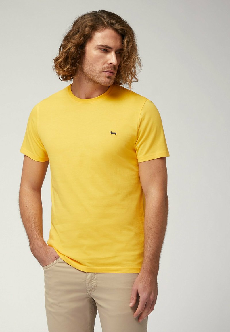 T-shirt gialla a maniche corte realizzata in cotone, con scollatura a girocollo e un piccolo logo di un cane nero sul lato sinistro del petto. Tessuto morbido.