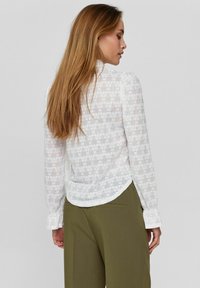 Witte kanten blouse met lange mouwen, bloemmotief en gerimpelde manchetten, gecombineerd met olijfgroene broek met een ronde zoom.