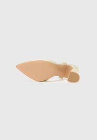 Beige hoge hak met een gemêleerde band en een puntige neus. De buitenzool is glad met een lichtbruine tint en een subtiel grippatroon.