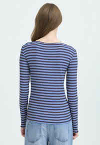Langærmet top med blå og brune vandrette striber, ribbet tekstur og en bred, rund halsudskæring. Båret over lyseblå jeans.
