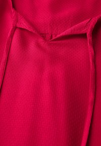 Tessuto atletico rosso che mette in evidenza un motivo testurizzato e traspirante. Il design presenta un collo a V e cuciture a vista per una maggiore struttura.