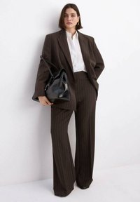 Completo a righe marrone con pantaloni a gamba larga e blazer doppiopetto, abbinato a una camicia bianca e una borsa a mano in pelle nera.