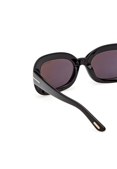 Lunettes de soleil œil de chat noires brillantes avec des verres teintés foncés, une bande argentée sur la branche et une petite plaque logo dorée à l'extrémité de la branche.