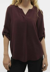 Blusa bordeaux con scollo a V e maniche arrotolate, realizzata in tessuto testurizzato; vestibilità comoda con orlo leggermente più lungo sul retro.
