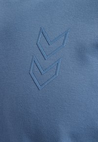 Blå bomulls-T-shirt med en texturerad, ljusblå triangulär logotypdesign på framsidan. Tyget verkar slätt och något elastiskt.