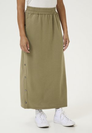 Olijf groene maxi rok met een elastische tailleband, zijknopen en een gladde textuur, gecombineerd met witte hoge sneakers.