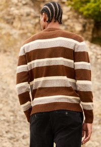 Maglione a righe marrone e beige con orlo a coste, realizzato in materiale morbido, abbinato a pantaloni scuri, visto da dietro.