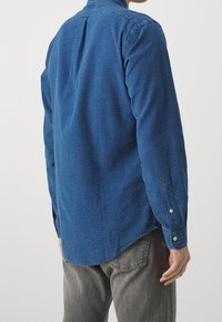 Blauw textuurshirt met een button-down kraag, zijplooidetail en knoopmanchetten, gecombineerd met grijze broek.