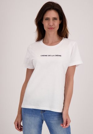 Witte katoenen t-shirt met korte mouwen en een ronde hals, versierd met de tekst "CRÈME DE LA CRÈME" in het zwart over de borst.