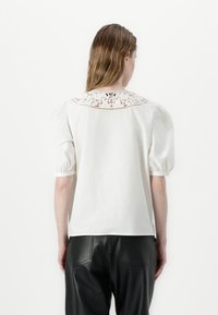 Blouse blanche à manches courtes avec un col en dentelle et des manches bouffantes, associée à un pantalon en cuir noir. Texture lisse et design décontracté.