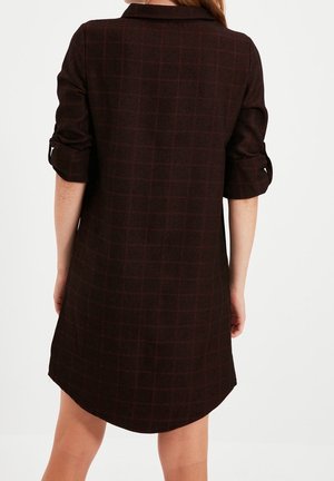 Bruine geruite overhemdjurk met een kraag, opgerolde mouwen en een gebogen zoom. De stof heeft een getextureerd patroon.