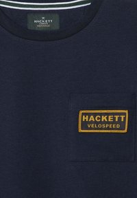 Námornícke tričko s okrúhlym výstrihom, s náprsným vreckom a žltou vyšívanou nálepkou s nápisom "HACKETT VELOSPEED." Bavlnená tkanina, hladká štruktúra.