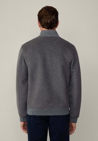 Chaqueta de mezcla de lana gris con un diseño estructurado, que presenta un cuello alto y puños acanalados. La tela tiene una textura suave y un brillo sutil.