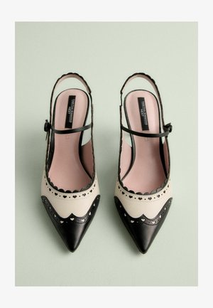 Zwart-witte slingback hakken met puntige neuzen, van leer, met geschulpte randen, een doorboord hartontwerp en een dunne enkelband.