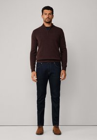 Maglione zip con collo a lupetto marrone scuro, camicia blu sotto, abbinato a jeans blu scuro e scarpe stringate marroni. Design semplice e aderente.