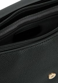 Schwarzes strukturiertes Lederinnere der Tasche mit einem Reißverschluss, das eine glatte schwarze Innenauskleidung und einen Beschlag in Goldton aufweist.