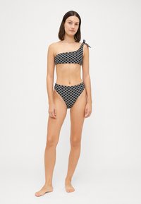 Fekete-fehér mintás bikini; egyvállú felső, megkötős részlettel, magas derekú alsó. Simaság, testhezálló fazon, minimalista stílus.