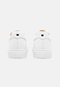 Weiße Leder-Sneaker mit einer strukturierten weißen Gummisohle, kontrastierendem schwarzen Logo an der Ferse und einem glatten, minimalistischen Design.