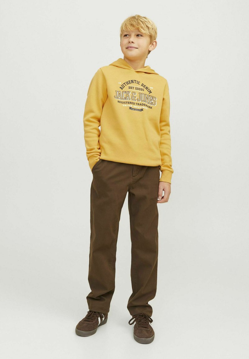 Felpa gialla con logo stampato, abbinata a pantaloni marroni e sneakers marroni. Tessuto morbido, vestibilità comoda e cappuccio con cordoncino.
