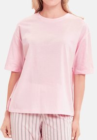 Lichtroze katoenen T-shirt met korte mouwen, ronde halslijn en zijsplitten. Effen textuur, relaxte pasvorm en minimale ontwerpelementen.