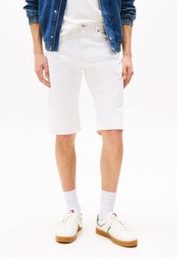 Hvite denimshorts med rett passform, med fem lommer og en lett oppbrett nederst, sammen med hvite joggesko og ripete sokker.