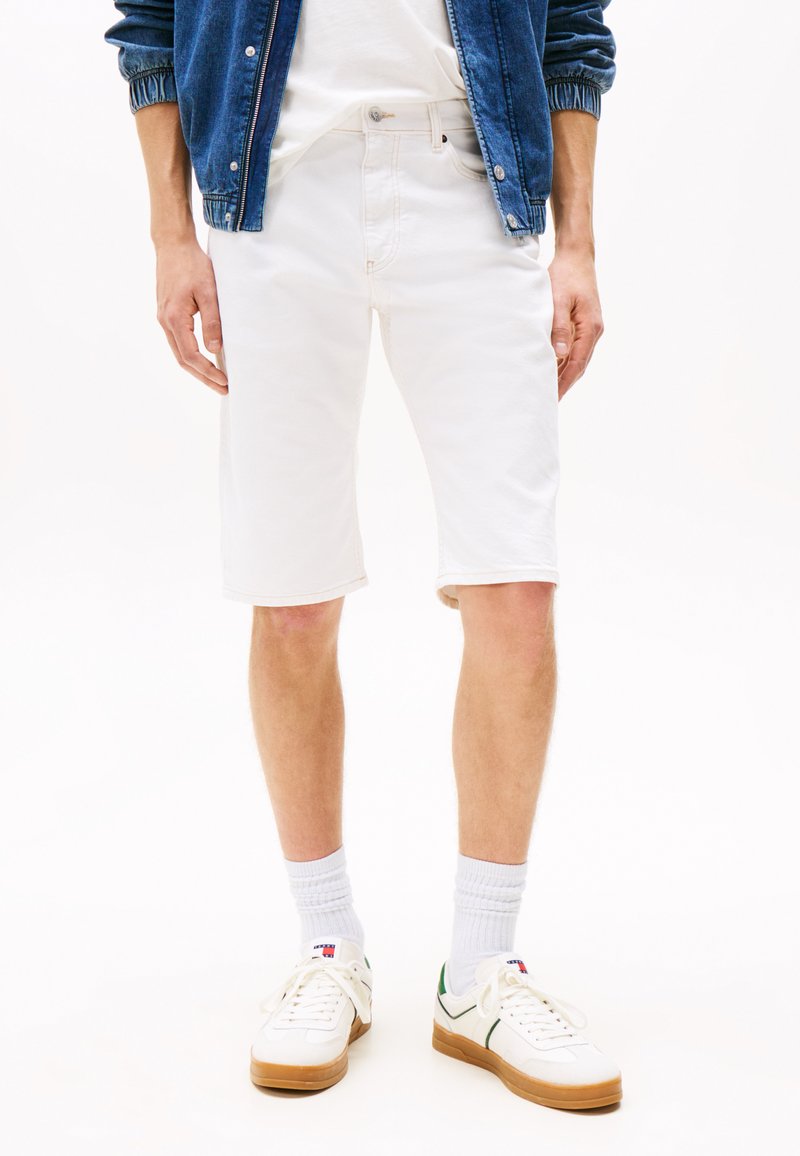 Hvite denimshorts med rett passform, med fem lommer og en lett oppbrett nederst, sammen med hvite joggesko og ripete sokker.