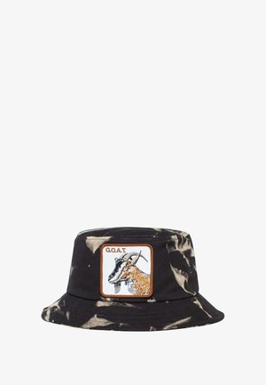 Cappello bucket tie-dye nero e crema con una toppa quadrata che presenta un design di capra e il testo "G.O.A.T" ricamato in filo marrone. Materiale in cotone.