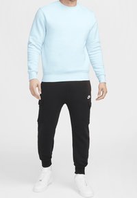 Felpa azzurra chiara a maniche lunghe, abbinata a pantaloni cargo neri con tasche e sneakers bianche. Design semplice e casual.
