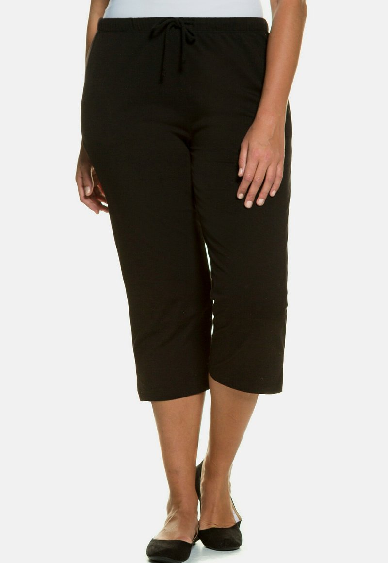 Zwarte capri-broek van zacht materiaal, met een elastische tailleband en trekkoord, en een recht model dat net onder de knie eindigt.