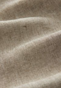 Tela tejida de color marrón claro con una sutil textura, que muestra un fino patrón de pequeñas fibras espaciadas uniformemente. Apariencia suave y flexible.