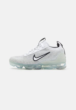 Biały dzianinowy sneakers Nike z czarnym logo swoosh, przezroczystą podeszwą typu bubble oraz czarnymi zaczepami na języku i pięcie, widziany z boku.