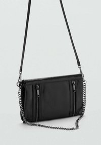 Svart fusk läder crossbody-väska med två dragkedjefickor, en kedjeaxelrem och en slät yta. Kompakt rektangulär form.