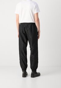 Černé nylonové kalhoty s texturovaným povrchem, elastickým pasem a manžetami. V kombinaci s jednoduchým bílým tričkem a černými botami.