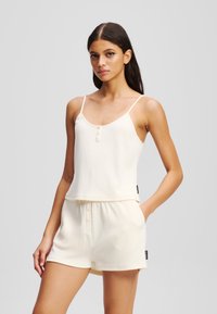 Valkoinen ribattua loungemekko, joka koostuu säädettävillä olkaimilla varustetusta topista, jossa on napitusyksityiskohtia, yhdistettynä elastisella vyötäröllä varustettuihin shortseihin.