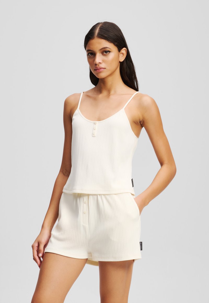 Valkoinen ribattua loungemekko, joka koostuu säädettävillä olkaimilla varustetusta topista, jossa on napitusyksityiskohtia, yhdistettynä elastisella vyötäröllä varustettuihin shortseihin.